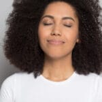A young Black woman smells the fresh air in her home after choosing an air cleaner or air purifier