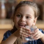 A young girl smiles as she drinks water purified to remove PFAS from drinking water