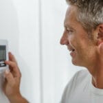 A man looks at his home thermostat to see if the auxiliary heat came on