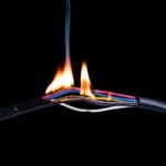 On a black background, flames emanate from exposed wires